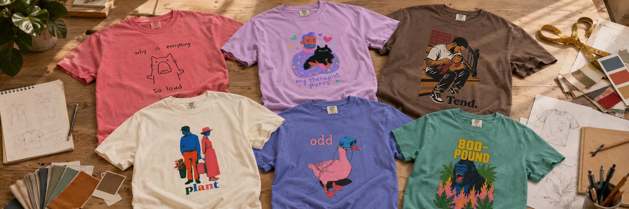 Six Muskrat & Rorke tees in garment-dyed colors laid out on a sunlit studio worktable